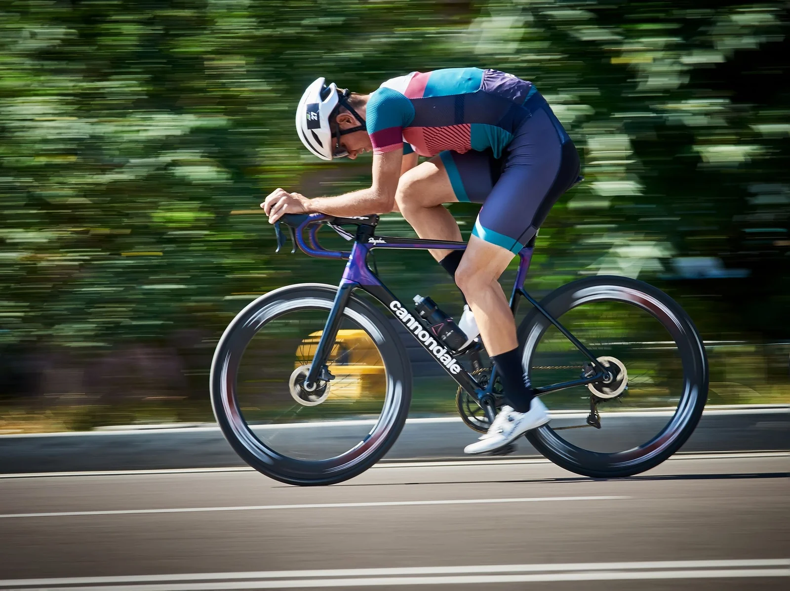 A cyclist in racing kit riding a road bicycle, seen from the side against a blurred green background.