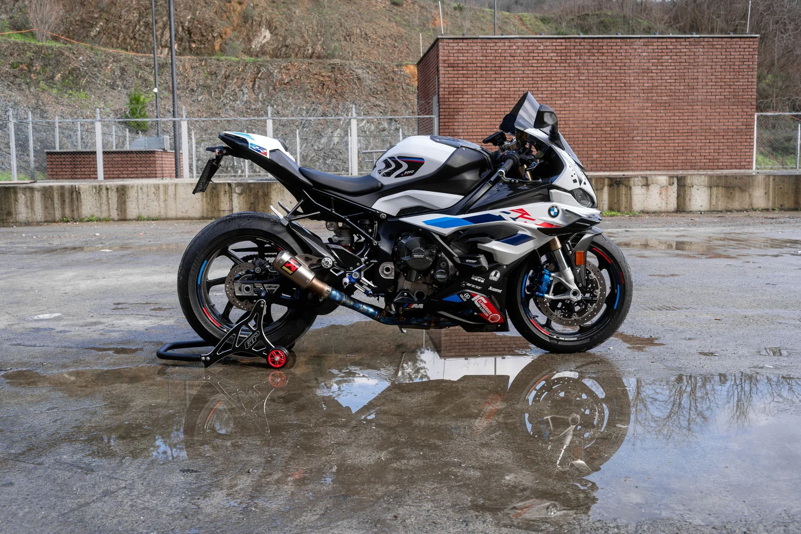 A white and blue sport motorcycle seen from the side, reflected in wet pavement.